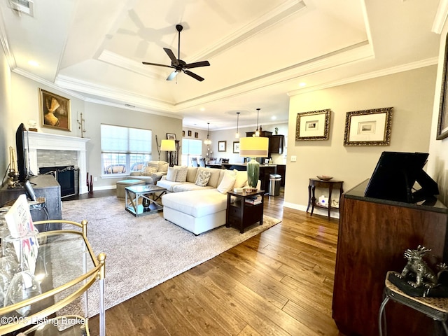 living area with a fireplace, a tray ceiling, wood finished floors, and visible vents