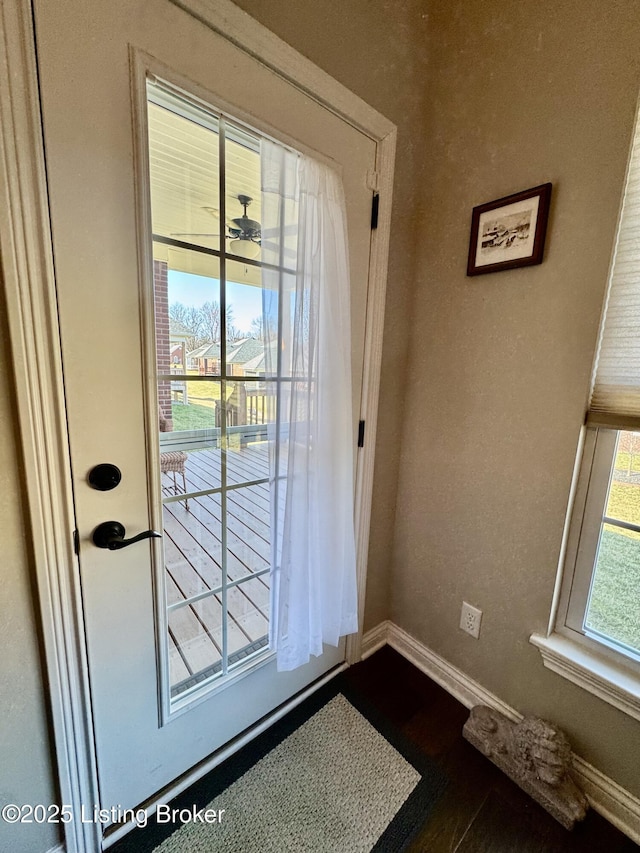 doorway with dark wood-style floors, ceiling fan, and baseboards