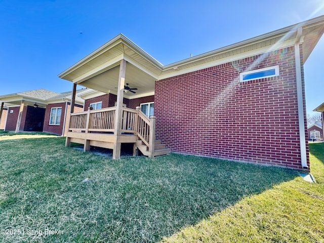 exterior space featuring brick siding, a lawn, a wooden deck, and ceiling fan