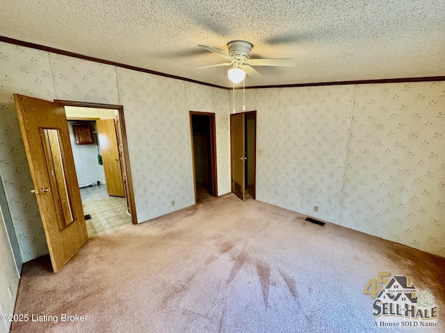 unfurnished bedroom with light carpet, a textured ceiling, ornamental molding, and wallpapered walls