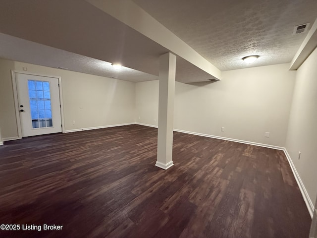 finished basement featuring visible vents, baseboards, a textured ceiling, and dark wood-style floors
