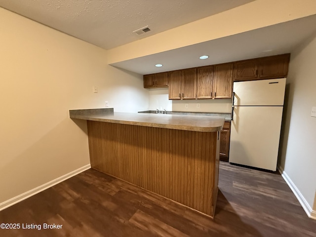 kitchen with visible vents, dark wood-type flooring, baseboards, a peninsula, and freestanding refrigerator