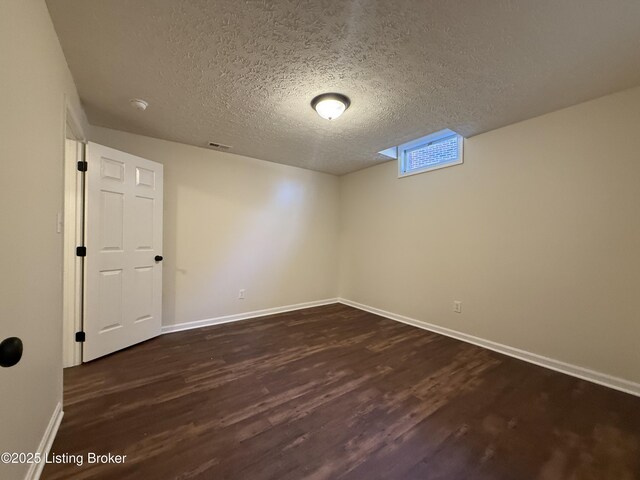 unfurnished room featuring visible vents, baseboards, dark wood-style flooring, and a textured ceiling