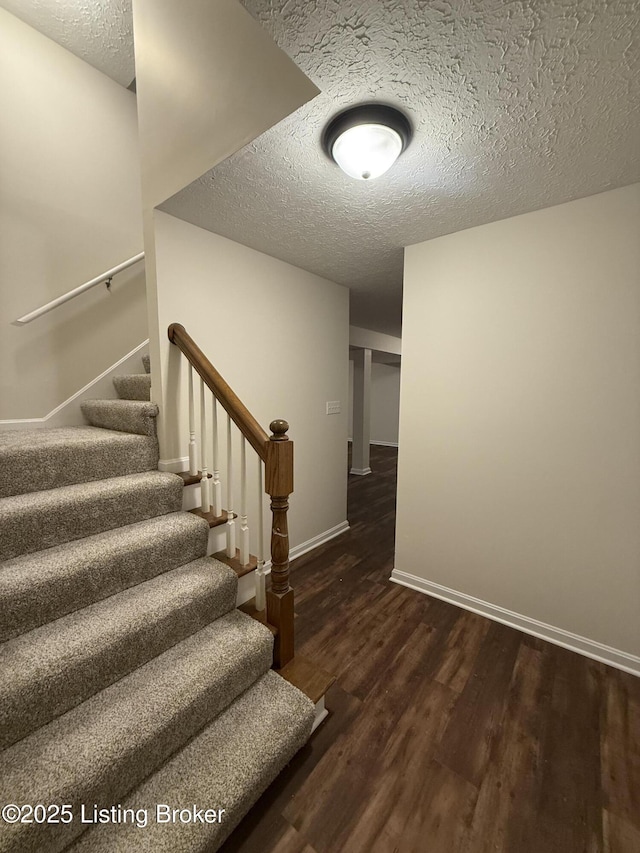 stairs with wood finished floors, baseboards, and a textured ceiling
