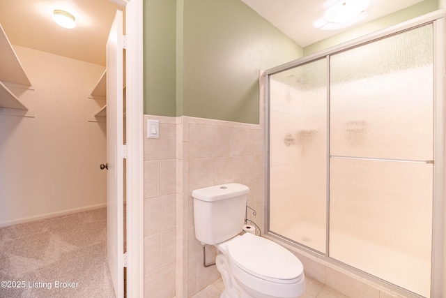 bathroom featuring tile walls, toilet, a wainscoted wall, and a shower stall