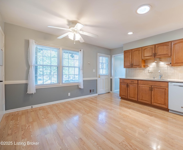 kitchen featuring decorative backsplash, brown cabinetry, white dishwasher, and a sink