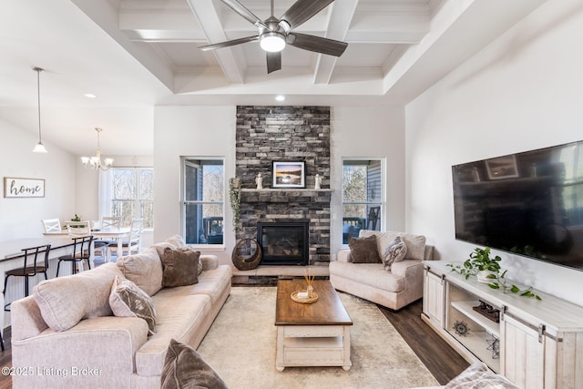 living area with beam ceiling, dark wood-type flooring, ceiling fan with notable chandelier, coffered ceiling, and a stone fireplace