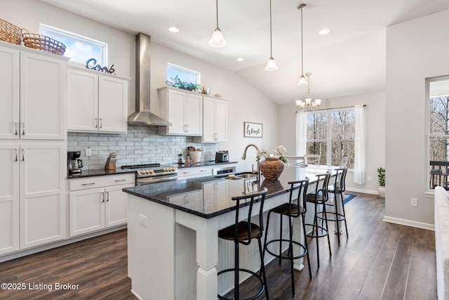 kitchen featuring a breakfast bar, a sink, tasteful backsplash, stainless steel electric range, and wall chimney range hood