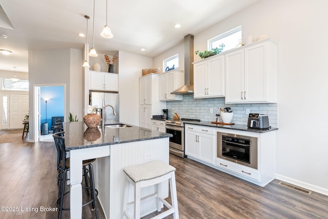 kitchen featuring visible vents, a sink, stainless steel appliances, wall chimney range hood, and backsplash