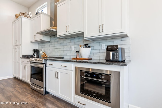 kitchen featuring dark wood-type flooring, tasteful backsplash, stainless steel range with electric cooktop, wall oven, and wall chimney range hood