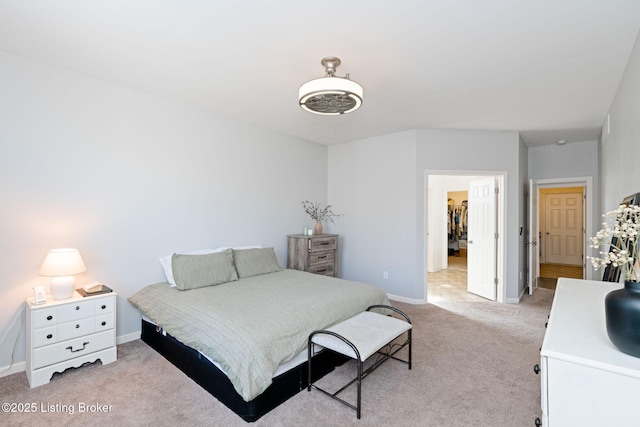 bedroom featuring a walk in closet, light colored carpet, and baseboards