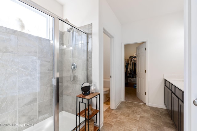 bathroom with a spacious closet, baseboards, toilet, a stall shower, and vanity