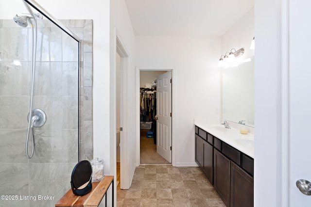 bathroom featuring baseboards, tiled shower, double vanity, a sink, and a walk in closet