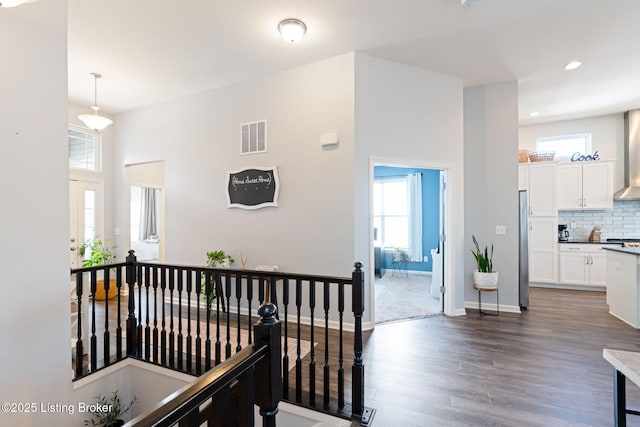 hallway with dark wood-style floors, an upstairs landing, visible vents, and a healthy amount of sunlight