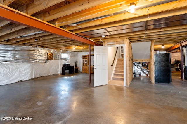 below grade area featuring stairway and freestanding refrigerator