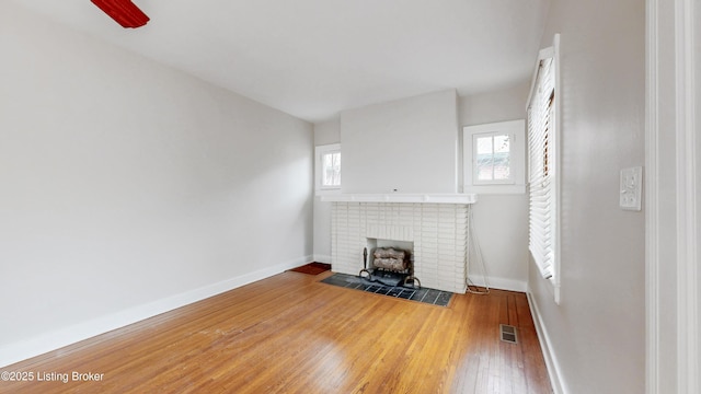 unfurnished living room with visible vents, baseboards, hardwood / wood-style floors, a fireplace, and a ceiling fan