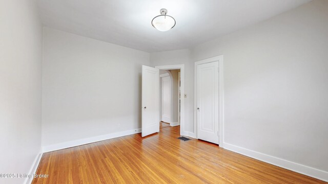 empty room with light wood-type flooring, visible vents, and baseboards