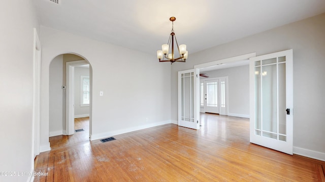 unfurnished room featuring visible vents, baseboards, arched walkways, french doors, and light wood-type flooring