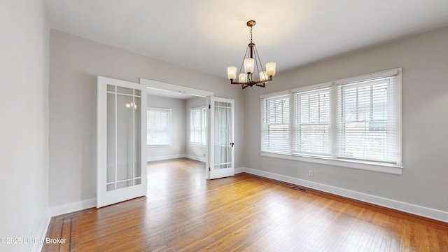 empty room with baseboards, wood finished floors, visible vents, and a chandelier