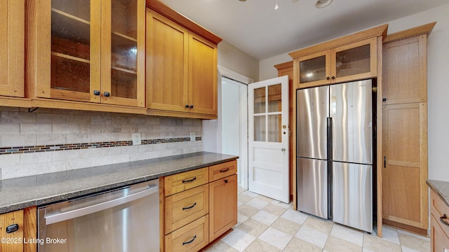 kitchen featuring stainless steel appliances, glass insert cabinets, tasteful backsplash, and dark stone counters