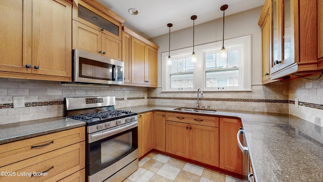 kitchen with a sink, decorative backsplash, glass insert cabinets, appliances with stainless steel finishes, and decorative light fixtures