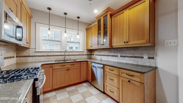 kitchen featuring pendant lighting, a sink, stainless steel appliances, brown cabinetry, and glass insert cabinets