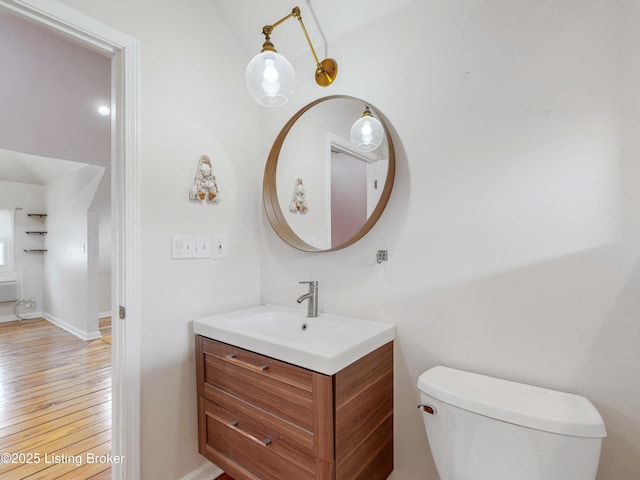 half bathroom featuring vanity, toilet, baseboards, and hardwood / wood-style floors