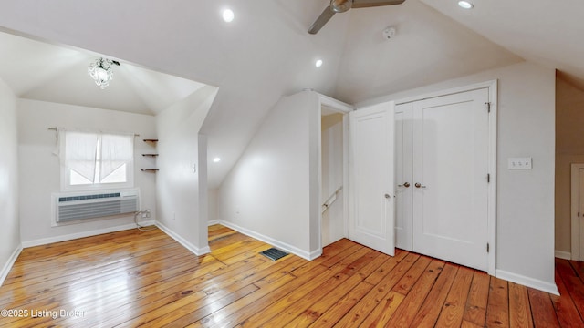 additional living space featuring lofted ceiling, a wall unit AC, visible vents, and light wood-type flooring