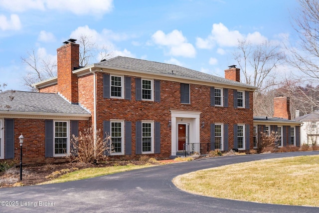 view of front of house with a front lawn, brick siding, roof with shingles, and a chimney