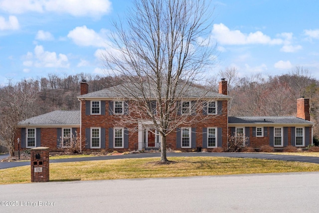 view of front facade featuring brick siding, a chimney, and a front lawn