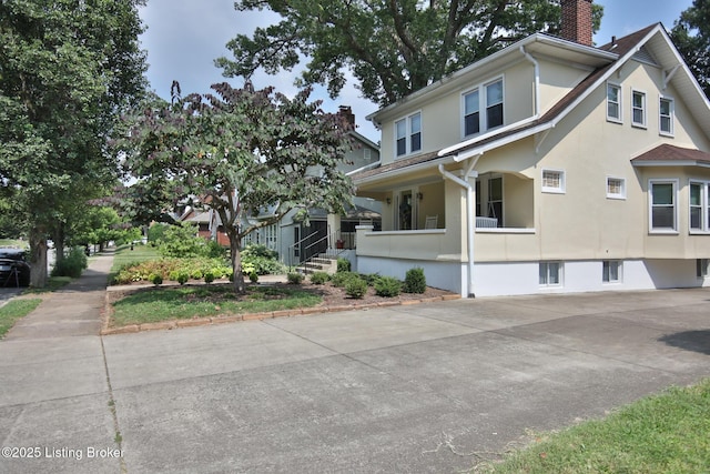 view of front facade featuring stucco siding, a porch, and a chimney