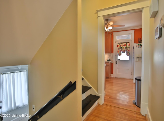 hallway with an upstairs landing, light wood-type flooring, and ornamental molding