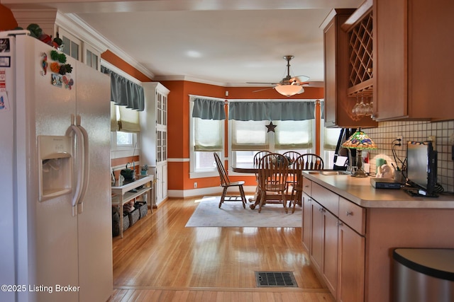 kitchen featuring visible vents, tasteful backsplash, light wood-style floors, white fridge with ice dispenser, and crown molding