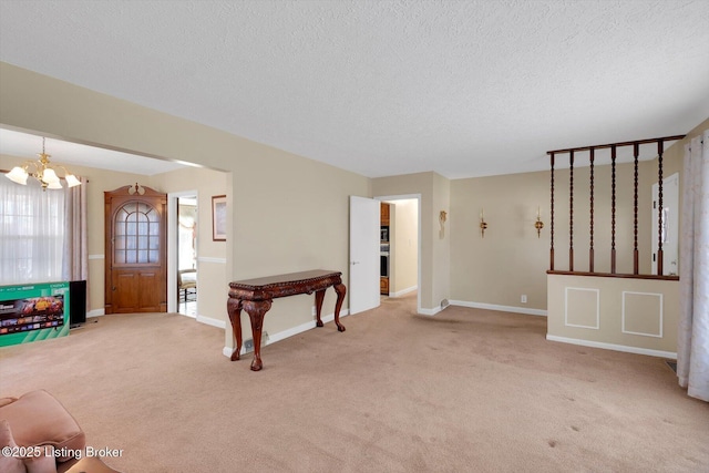 unfurnished living room featuring a notable chandelier, light colored carpet, baseboards, and a textured ceiling