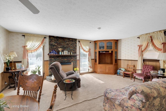 carpeted living room featuring wallpapered walls, a textured ceiling, plenty of natural light, and wainscoting