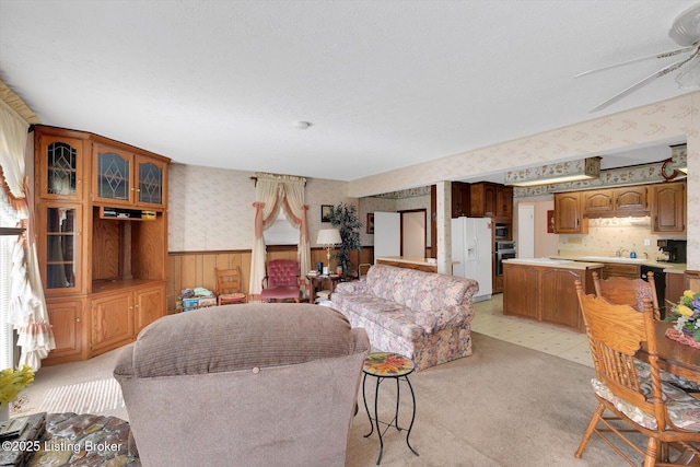 living area with light floors, ceiling fan, wainscoting, and wallpapered walls