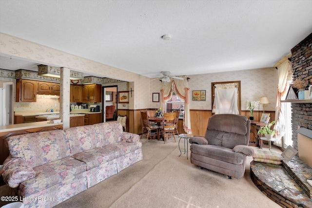 living room featuring wallpapered walls, a wainscoted wall, light carpet, a fireplace, and a ceiling fan