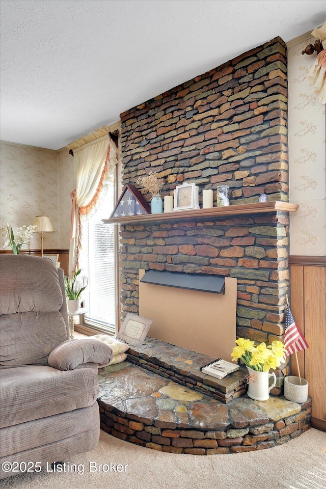 living room with carpet floors, wallpapered walls, a fireplace, wainscoting, and a textured ceiling