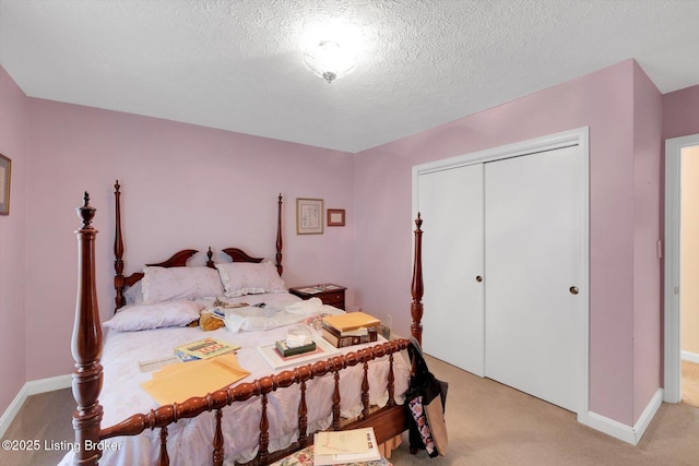 bedroom with a closet, baseboards, light colored carpet, and a textured ceiling