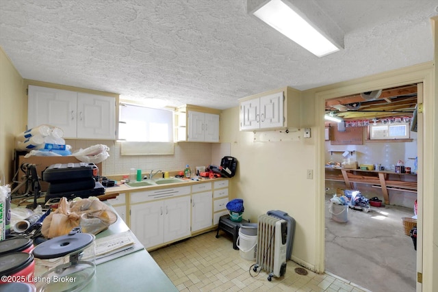 kitchen featuring tasteful backsplash, white cabinets, light countertops, and a sink