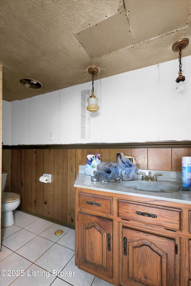 interior space with toilet, wooden walls, wainscoting, tile patterned flooring, and vanity