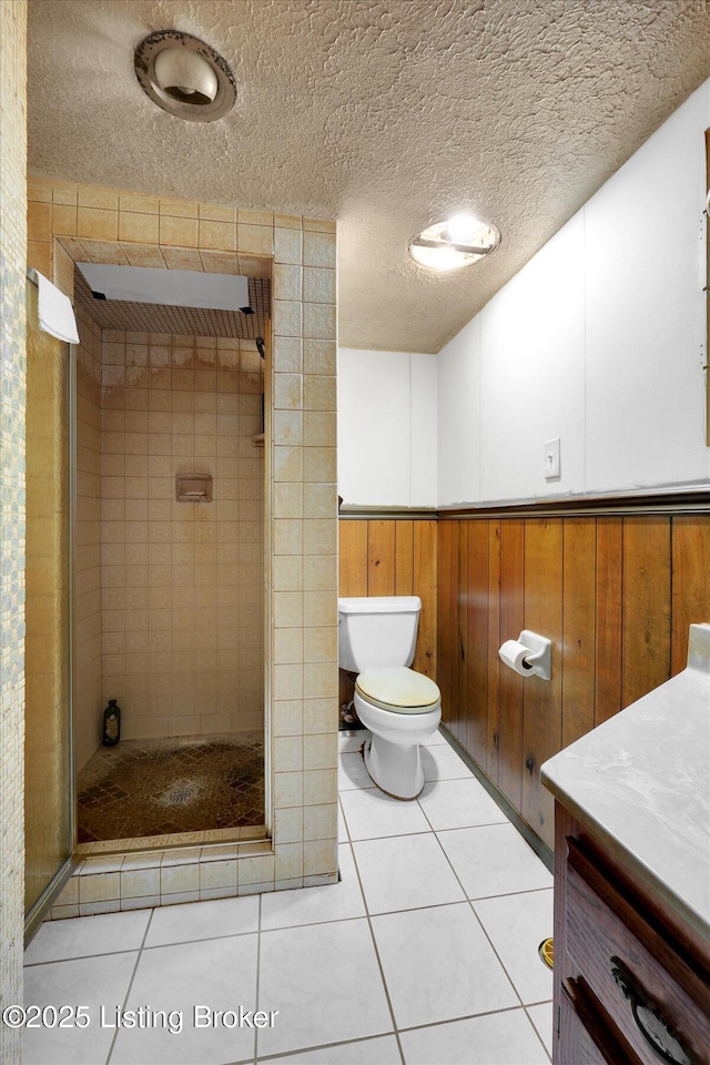 bathroom with wainscoting, a shower stall, a textured ceiling, tile patterned floors, and toilet