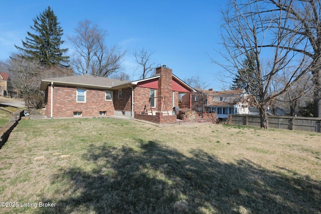 rear view of house with brick siding, a chimney, a yard, and fence