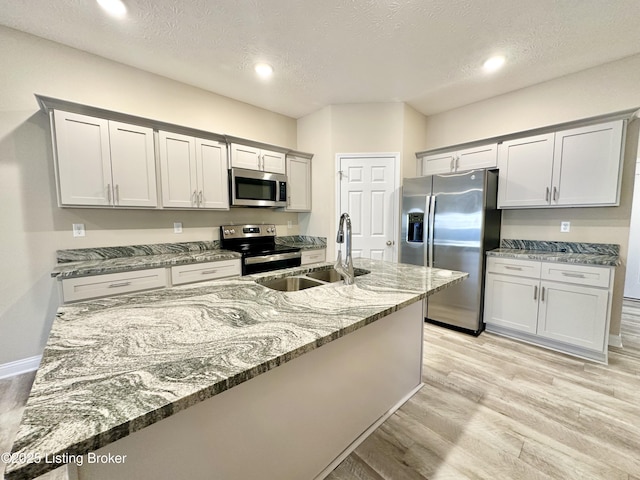 kitchen featuring light wood-type flooring, a sink, light stone counters, a textured ceiling, and appliances with stainless steel finishes