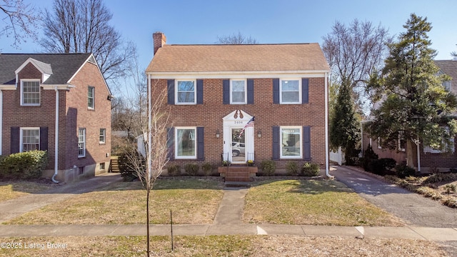 colonial inspired home with a front lawn, brick siding, driveway, and a chimney