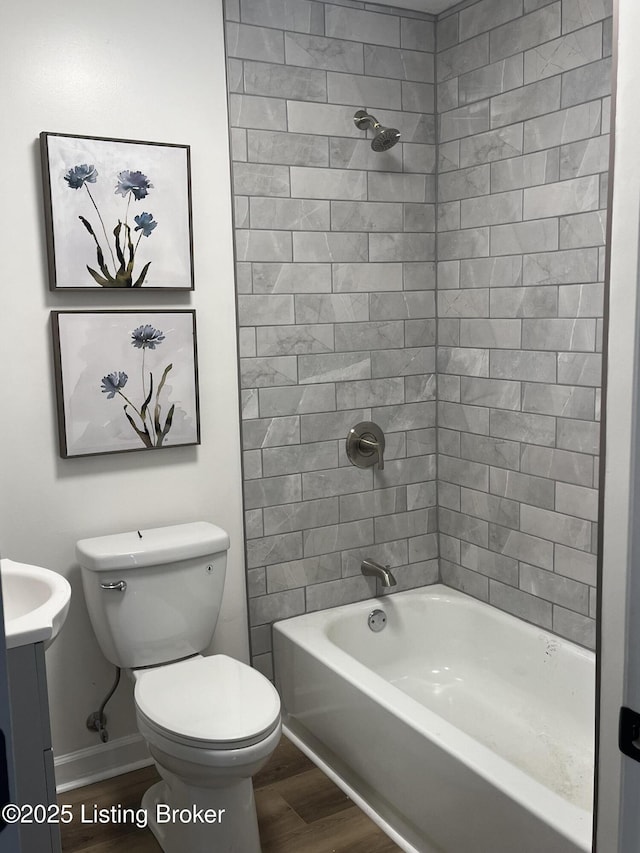 full bath featuring baseboards, toilet, vanity, wood finished floors, and washtub / shower combination