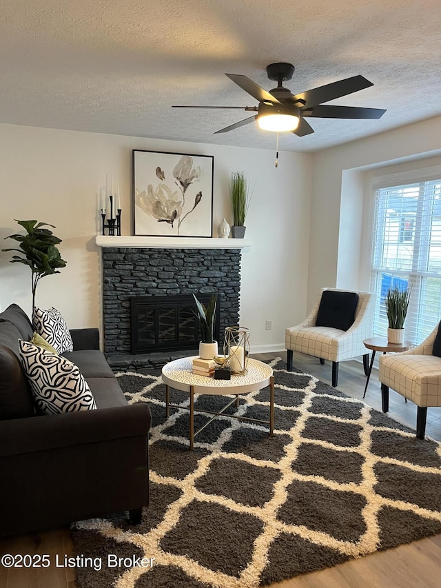 living room featuring wood finished floors, baseboards, a fireplace, ceiling fan, and a textured ceiling