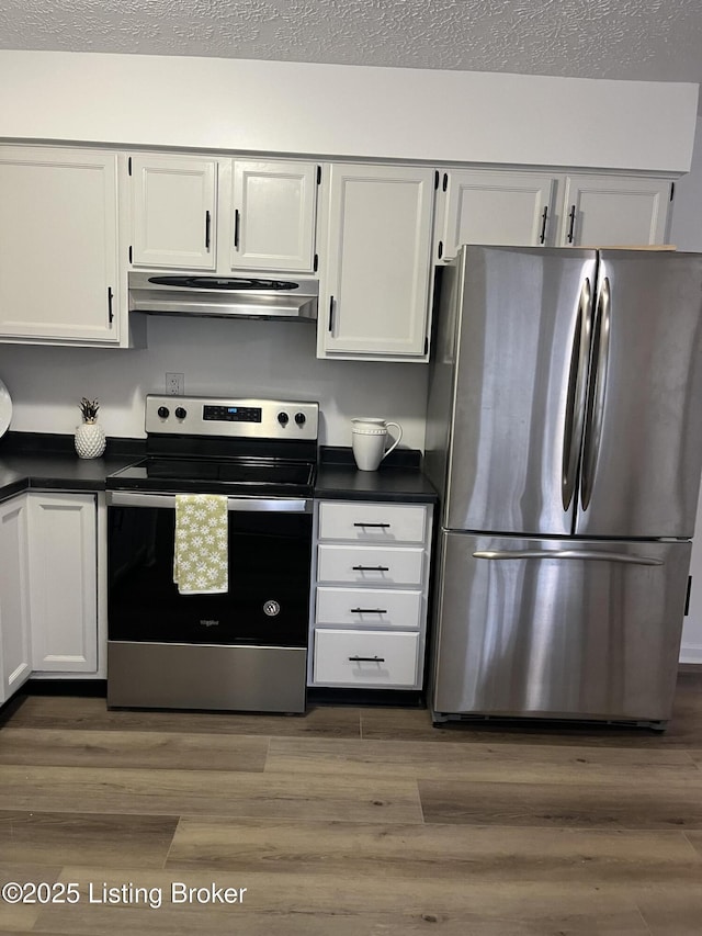 kitchen featuring under cabinet range hood, dark countertops, appliances with stainless steel finishes, and wood finished floors