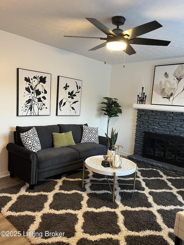 living area with a ceiling fan, a textured ceiling, wood finished floors, and a fireplace