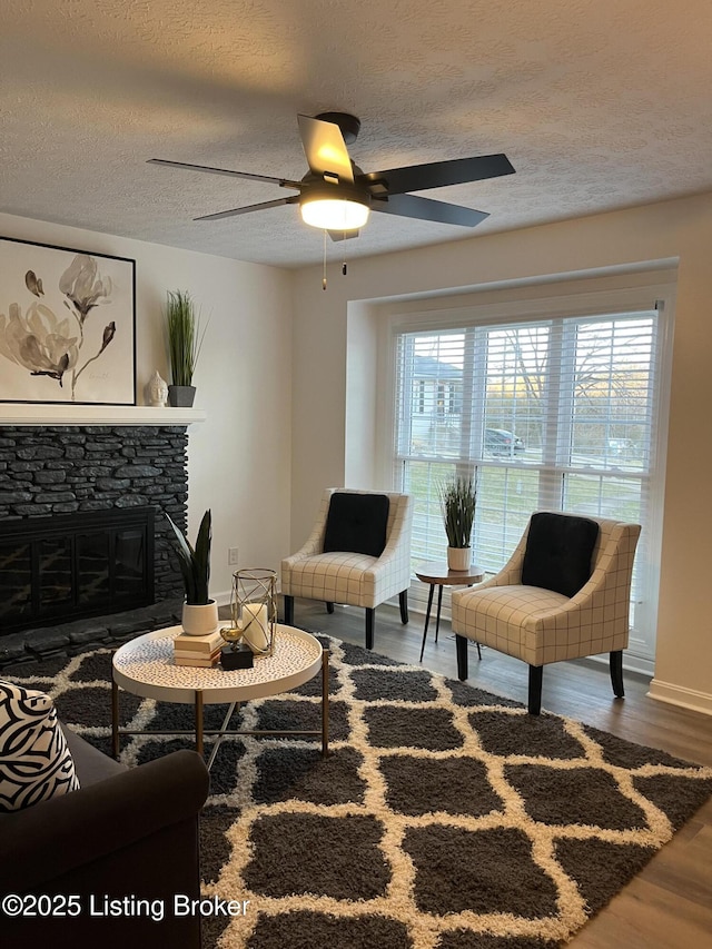 living room featuring ceiling fan, a textured ceiling, wood finished floors, and a fireplace